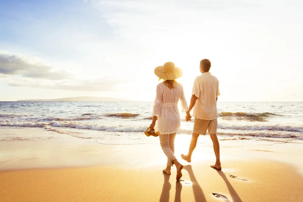 a romantic couple walking barefoot on the beach at sunset
