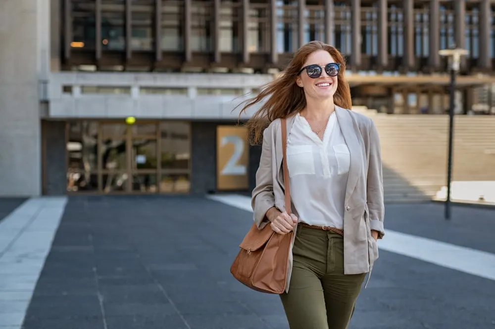 a smiling beautifully dressed woman with sunglasses walks down the street
