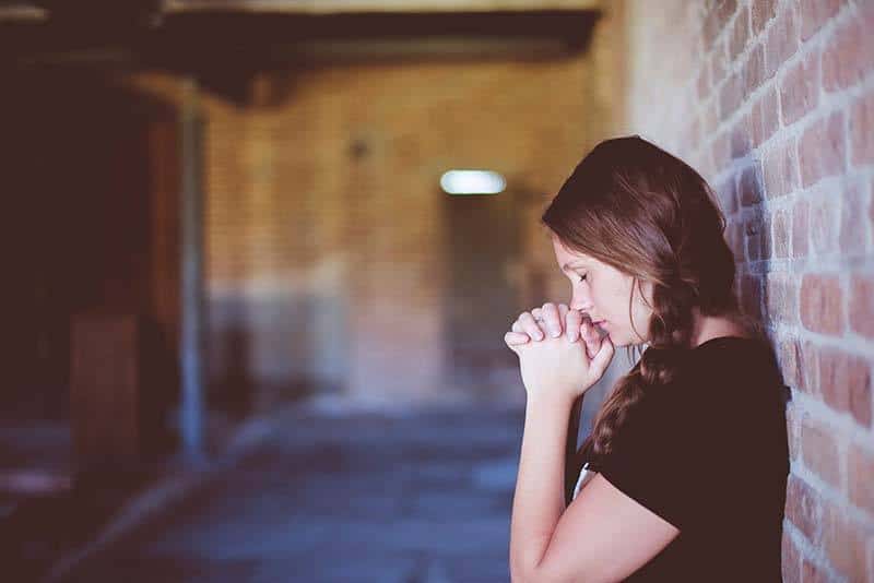 Chica apoyada en una pared rezando