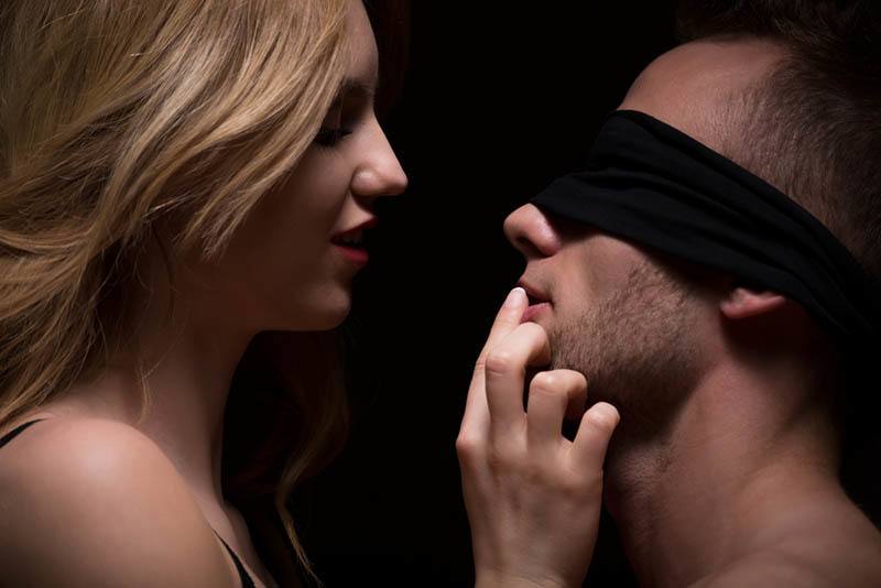 woman putting finger on man lips while he's eyes covered