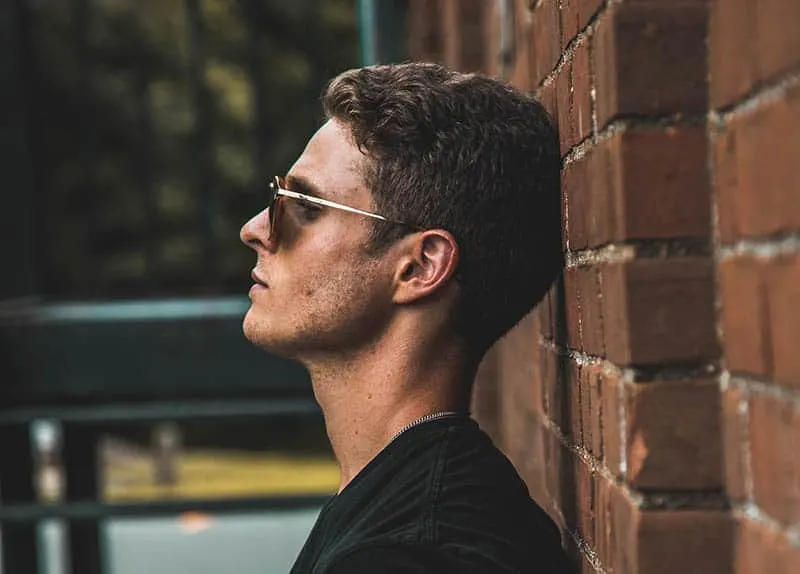 Man with sunglasses leaning his head against wall