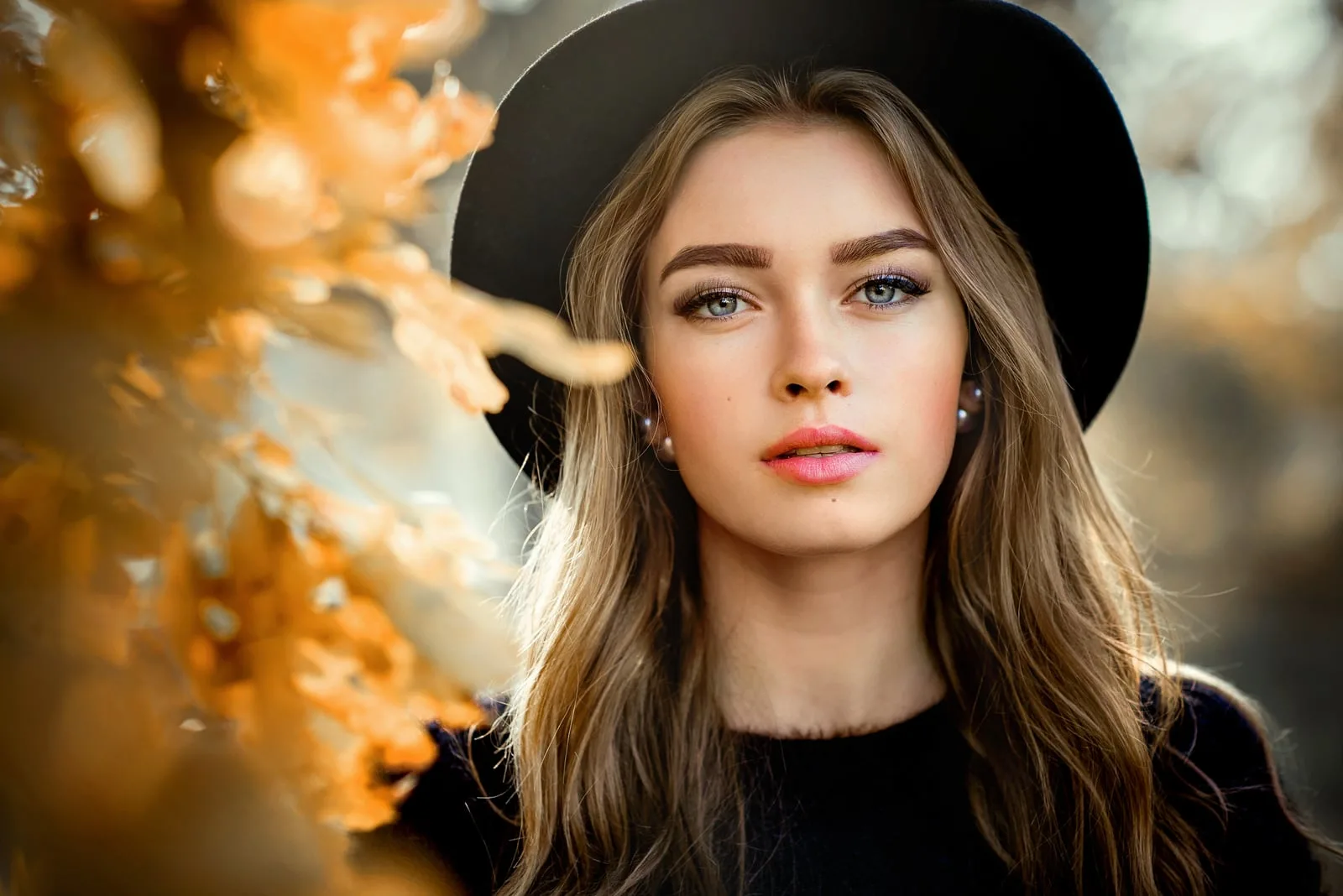 portrait of a Beautiful girl in a dark dress and black hat standing near colorful autumn leaves