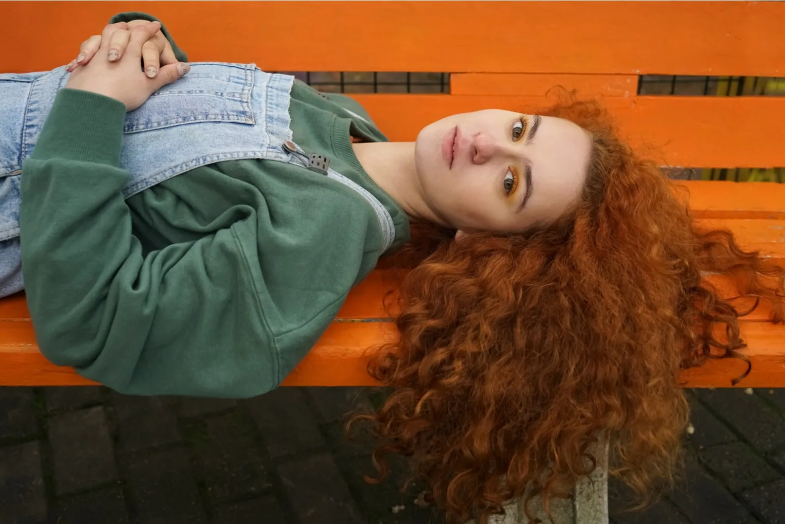 young redhead woman lying on orange bench in sunny autumn day