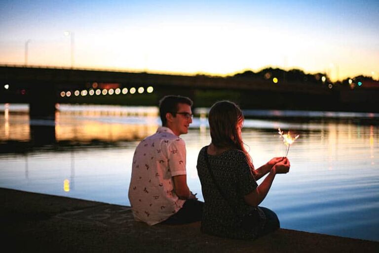 side of view of man and woman sitting together in front of lake