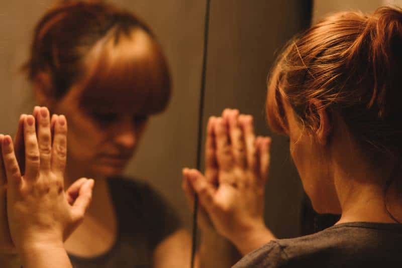 Sad and lonely woman looking at her reflection in the mirror