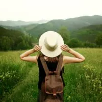woman traveler with backpack holding hat and looking at amazing mountains
