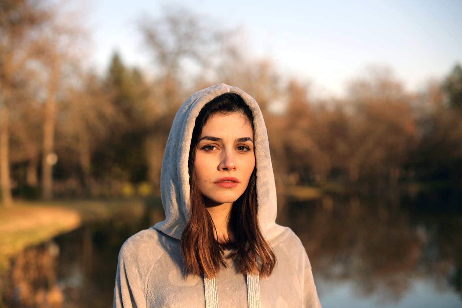 a portrait of a woman in a gray hoodie by the lake