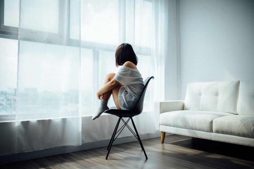 una chica triste sentada en una silla junto a la ventana