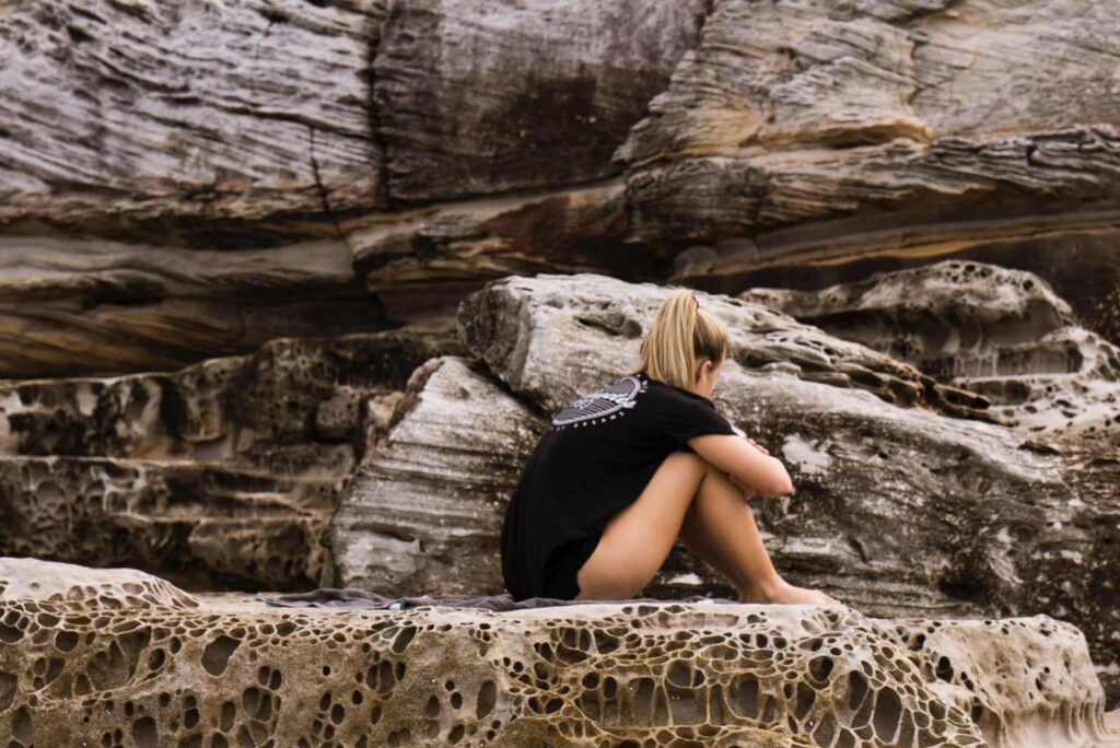 a sad girl sitting on a rock