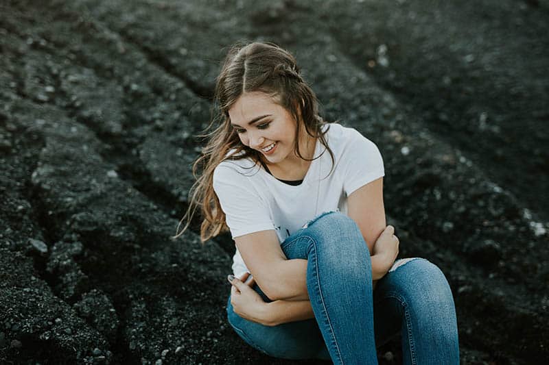 Happy young woman sitting on rocks hugging herself