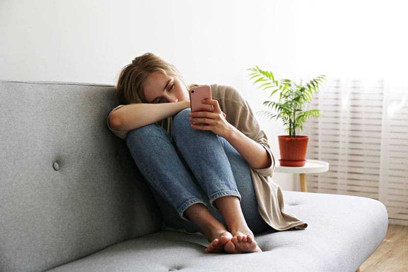 depressed woman holding her phone on the couch