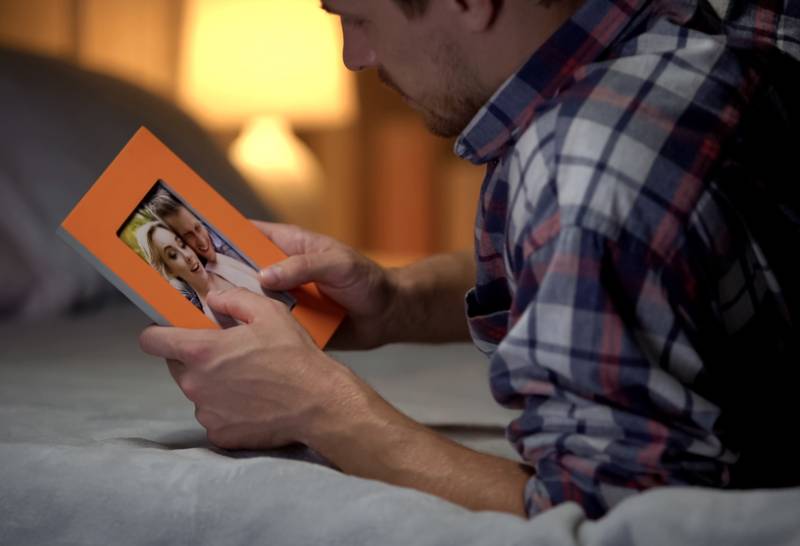 hombre desesperado tumbado en la cama y mirando una foto con su novia