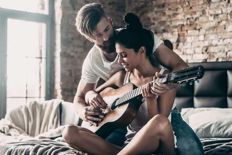 man teaching woman to play a guitar