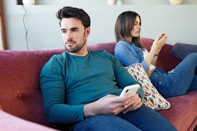 upset man holding phone and sitting next to woman