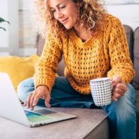 uma mulher sentada atrás de um computador portátil e com um café na mão