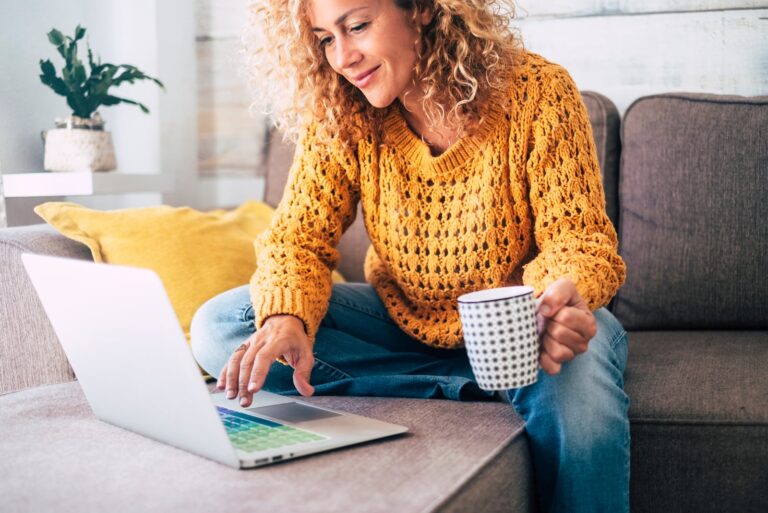 a woman sitting behind a laptop and holding a coffee in her hand
