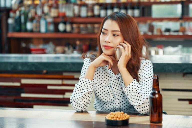 woman sitting at table with beer and talking on her phone