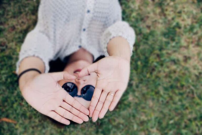 smiling woman wearing sunglasses and lying on grass field