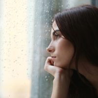 giovane donna triste che guarda attraverso una finestra piovosa