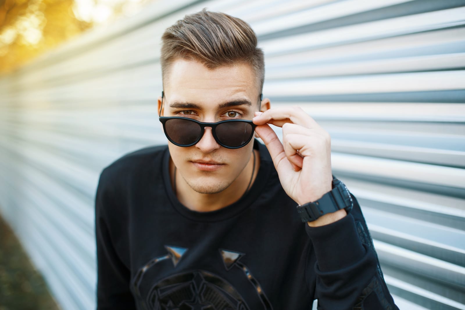 Hombre guapo joven con ropa elegante negro mirando a través de gafas de sol