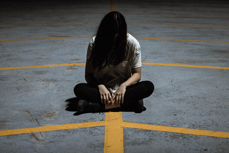 Girl sitting on parking lot with her head bowed down