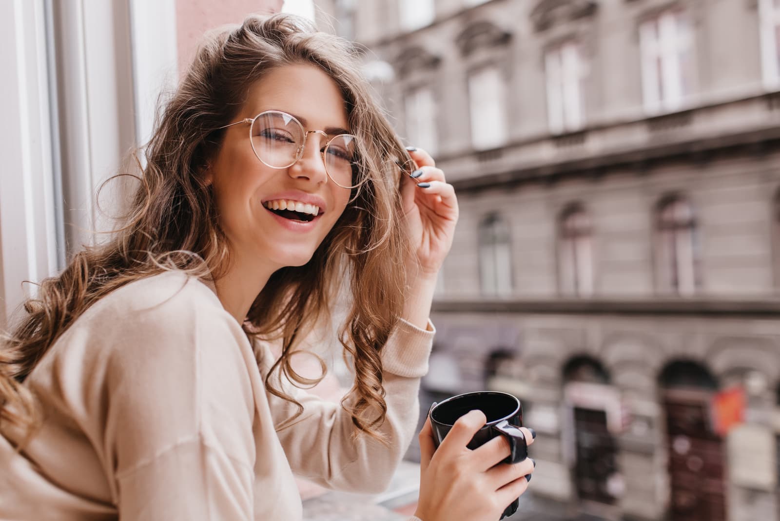 mulher bonita com cabelo encaracolado e óculos a segurar uma chávena de café