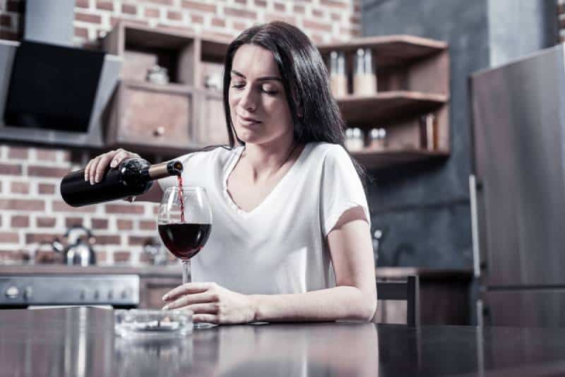 brunette sitting at the table and holding a bottle while pouring wine