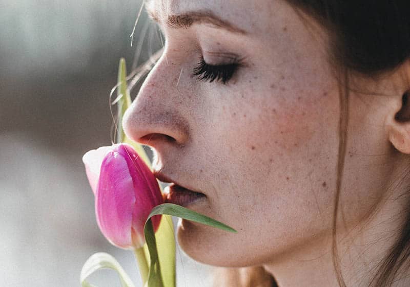 Mulher a cheirar uma flor com os olhos fechados