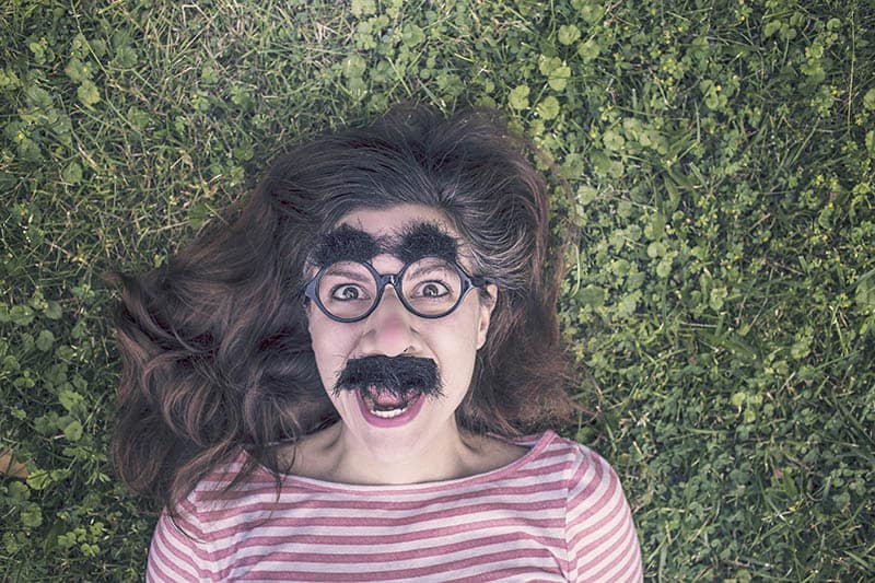 Chica tumbada en la hierba con una divertida máscara en la cara