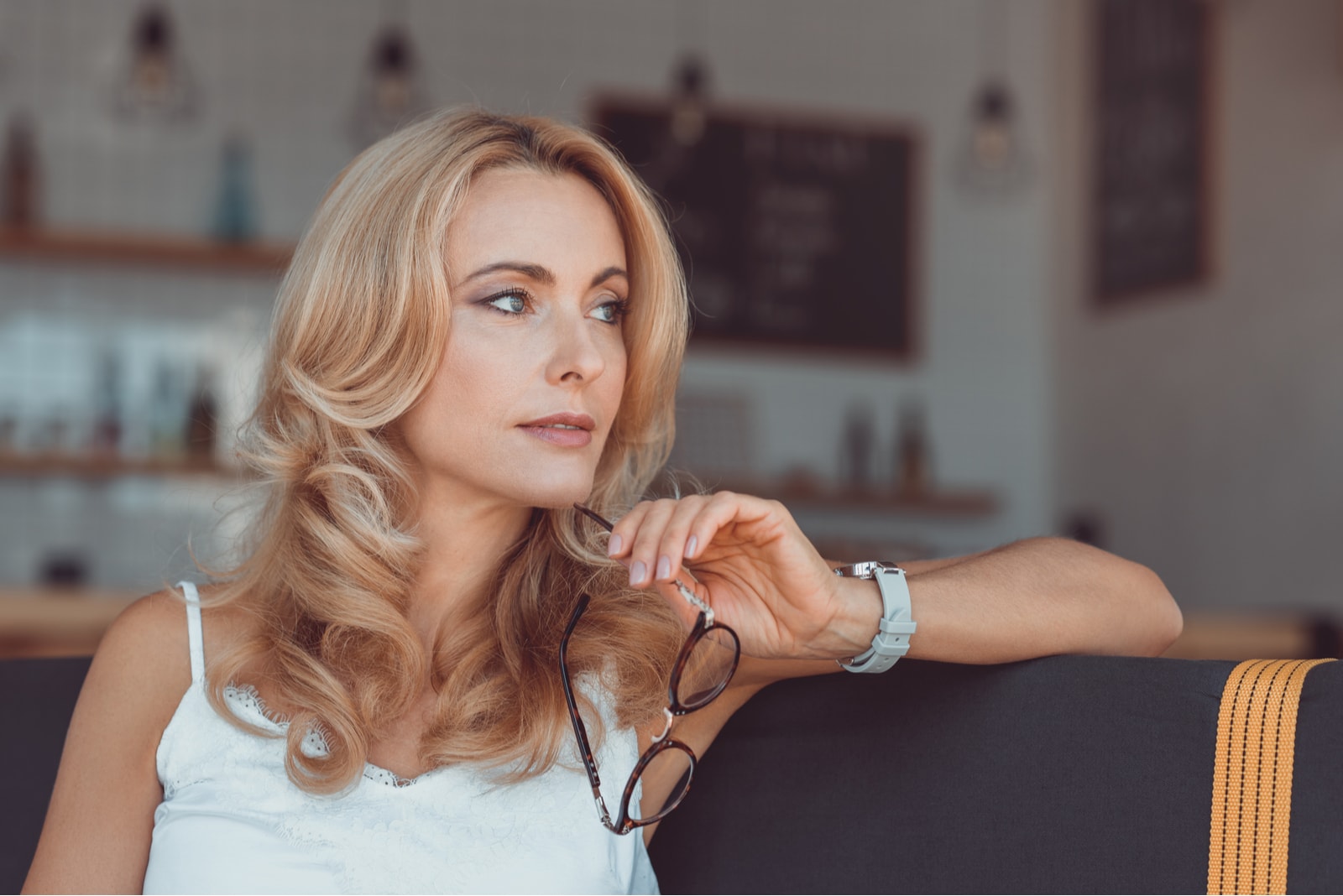 pensive woman holding eyeglasses and looking away