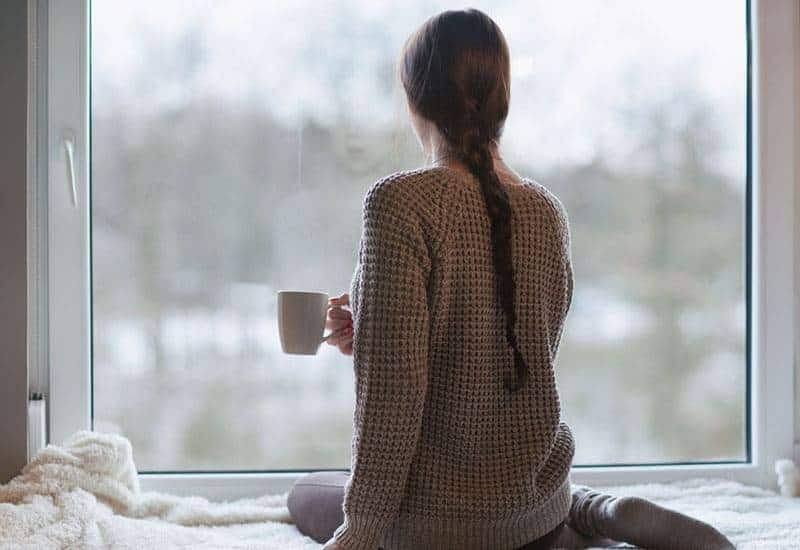 woman holding cup of tea and looking outside