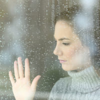 donna triste che si tiene per mano su una finestra piovosa