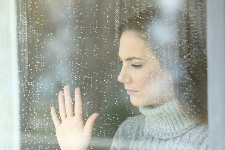 mulher triste de mão dada numa janela chuvosa