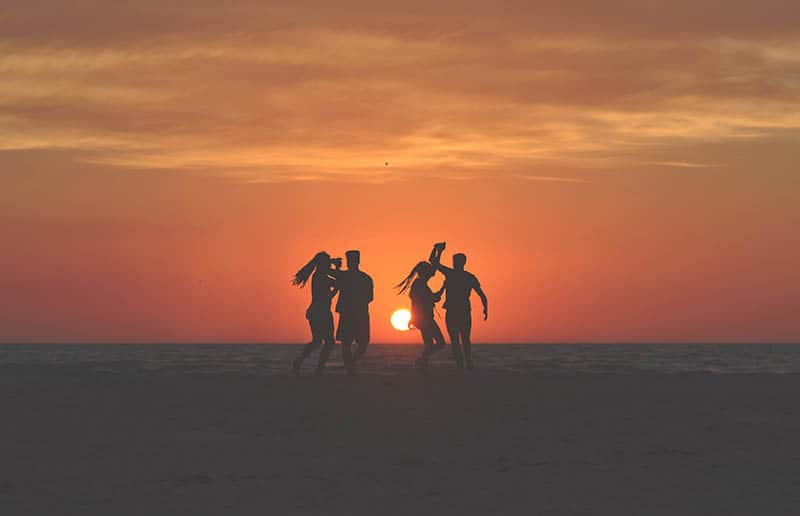 Young people dancing on beach at sunset