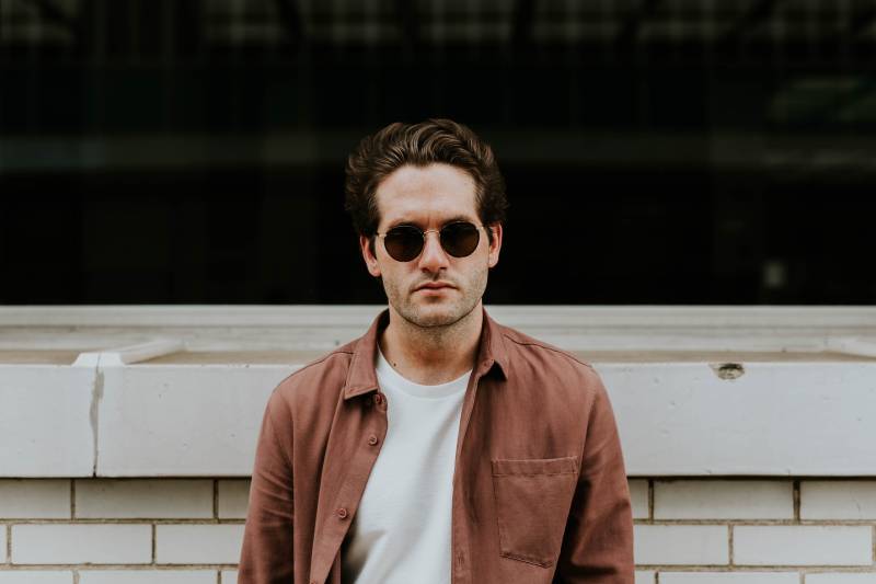 man with sunglasses and brown jacket standing outside
