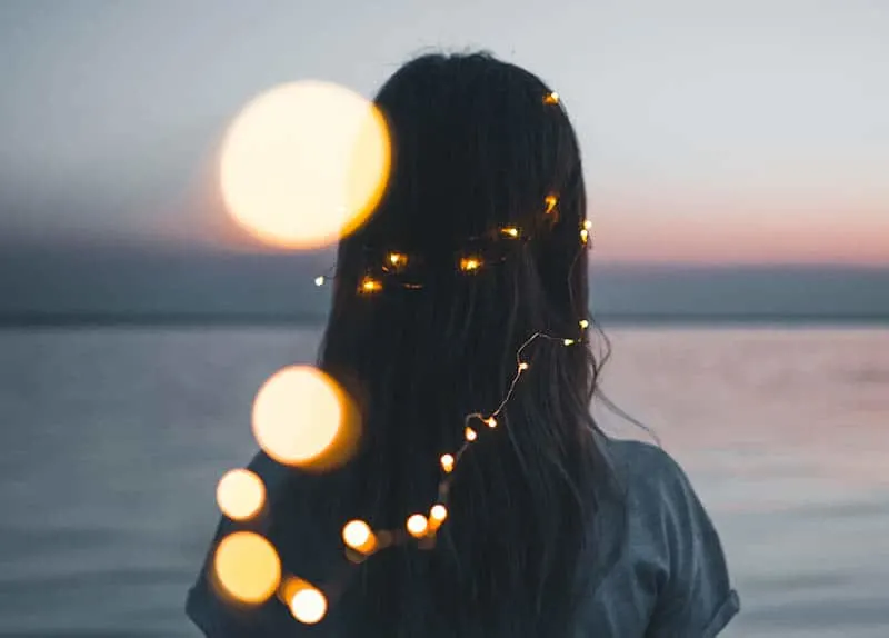 Girl looking into the horizon with string lights in her hair