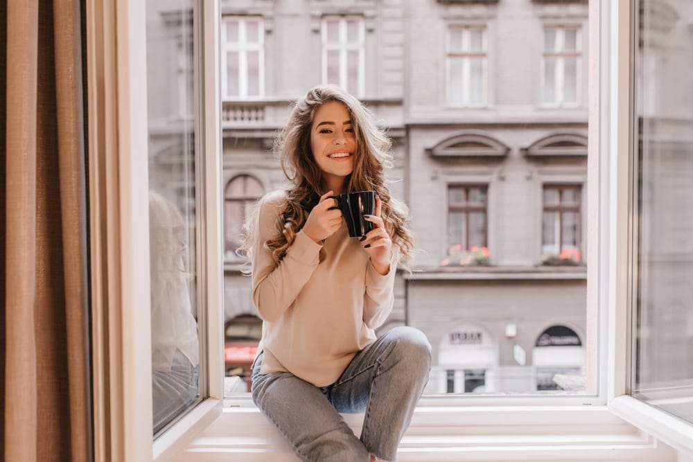 the woman is sitting at the window drinking coffee