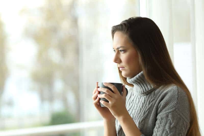 thinking woman holding cup of tea and looking outside