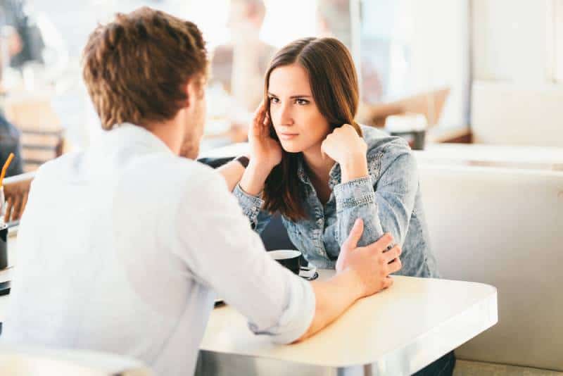 mulher a olhar desconfiada para um homem enquanto este lhe segura os braços num café