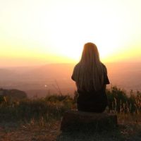 back view of woman sitting on mountain watching sunset