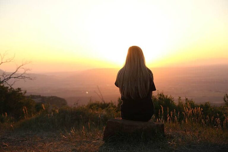 back view of woman sitting on mountain watching sunset