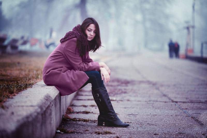 Una giovane donna deludente siede sul parapetto di pietra in questa giornata autunnale