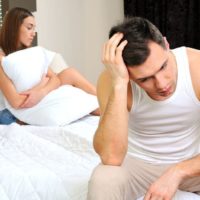 sad man sitting on bed apart from his girlfriend