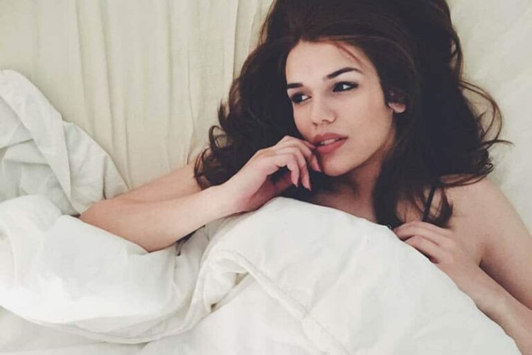 a woman with long black hair lies in bed