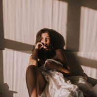 sexy brunette sitting on a bed covered with a white quilt