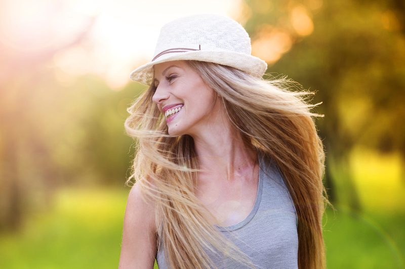 a woman with long blonde hair with a hat on her head laughs