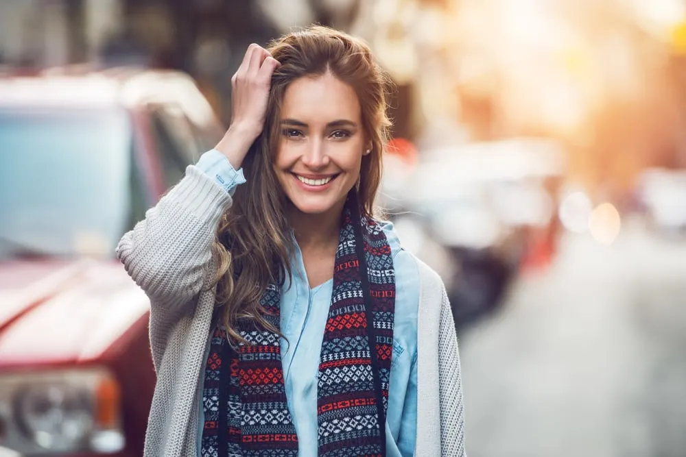 a woman with long brown hair walks down the street smiling