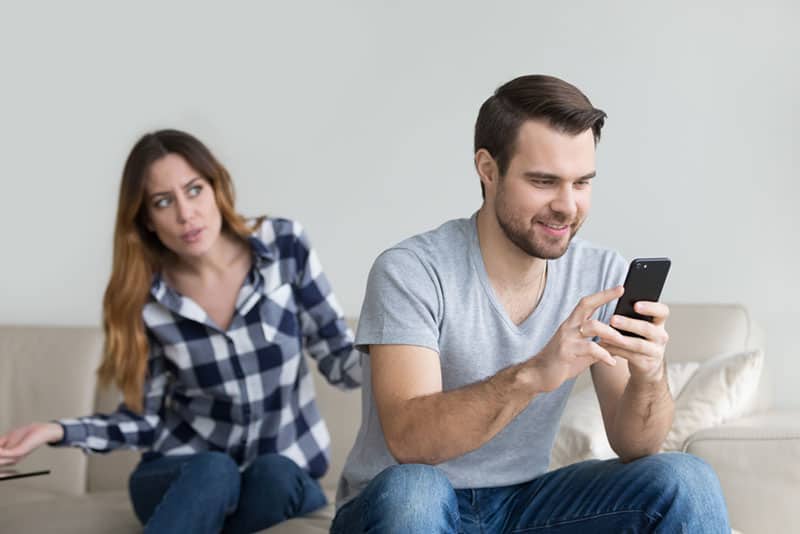 annoyed woman looking at man typing on phone