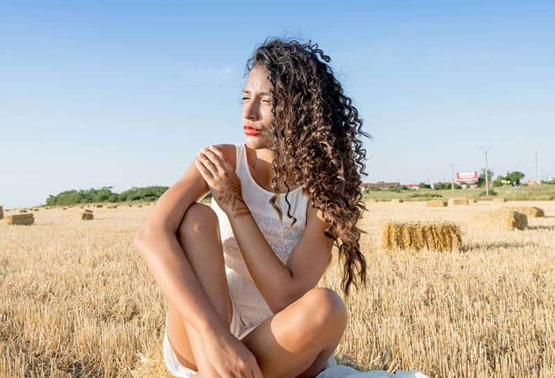 donna dai capelli ricci seduta su un campo marrone