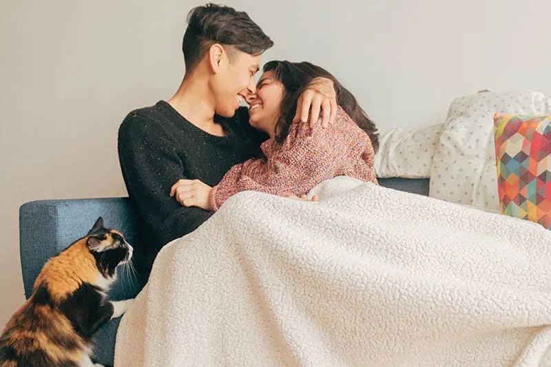 smiling couple cuddling under blanket at home